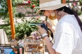 a brunette european woman in a white T-shirt and hat takes pictures of her goods at a street fair