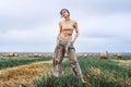 Brunette in fashionable clothes with bare shoulders standing in a wheat field on green grass. Woman holds her hands in pants Royalty Free Stock Photo