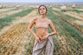 Brunette in fashionable clothes with bare shoulders standing in a wheat field on green grass. Woman holds her hands in pants Royalty Free Stock Photo