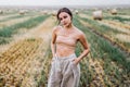 Brunette in fashionable clothes with bare shoulders standing in a wheat field on green grass. Woman holds her hands in pants Royalty Free Stock Photo