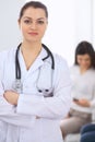 Brunette female doctor on the background of colleagues talking to each other in hospital. Physician is ready to help Royalty Free Stock Photo