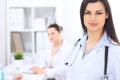 Brunette female doctor on the background of colleagues talking to each other in hospital. Physician is ready to help Royalty Free Stock Photo