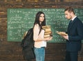 Brunette female student standing in front of green board with heap of books and huge backpack. Professor looking at