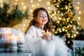 A brunette gilr in front of fur-tree and fireplace with candles and gifts. A girl making a wish. Christmas eve.