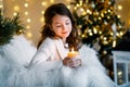 A brunette gilr in front of fur-tree and fireplace with candles and gifts. A girl making a wish. Christmas eve.