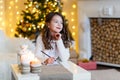 A brunette gilr in front of fur-tree writing a letter to santa claus. A girl dreaming. New year`s eve. Christmas