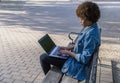 Brunette girl with afro hair works with her laptop sitting on a park bench on a spring day Royalty Free Stock Photo