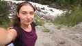 Brunette girl with a backpack travels through the mountains. Tired tourist on the background of mountains and a stormy river