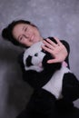 Portrait of a brunette girl in a black turtleneck holding big fluffy panda-toy against a gray wall