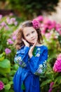 Brunette girl in a blue dress with ethnic embroidery in the garden of pink hydrangeas, the little girl is holding flowers Royalty Free Stock Photo