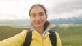 A brunette girl in a bright yellow jacket and with a backpack takes a selfie against the background of the beautiful Altai Royalty Free Stock Photo