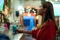 A brunette girl dressed in red at a bar counter with lights in the background. Party girl in a bar at night. Girl drinking a blue