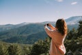 A girl takes a picture of the mountains and forests around her on a sunny day Royalty Free Stock Photo