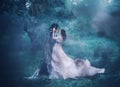 Brunette girl ghost and spirit of nightly mysterious cold blue forest, lady in white vintage lace dress with long flying Royalty Free Stock Photo