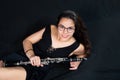 A brunette girl, with glasses, lying laughing and holding her clarinet music instrument isolated on a black background Royalty Free Stock Photo