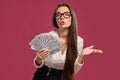 Brunette girl in glasses, wearing in a black short skirt and white blouse is posing holding a fan of hundred dollar Royalty Free Stock Photo