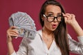 Brunette girl in glasses, wearing in a black short skirt and white blouse is posing holding a fan of hundred dollar Royalty Free Stock Photo