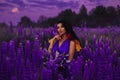 A brunette girl in a gradient haute couture dress standing among a blooming lupine field