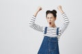 Brunette girl with hairbuns in striped top excited and glad to achieve victory, clenches fists, screams in excitement