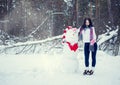 Brunette girl in hat and mittens sculpts a snowman