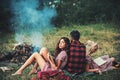 Brunette girl leaning on her boyfriend while reading book. Turn back guy looking at campfire. Young couple in love Royalty Free Stock Photo