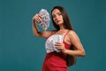 Brunette girl with a long hair, wearing a sexy red dress is posing holding a fan of hundred dollar bills against a blue Royalty Free Stock Photo