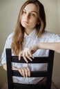 A brunette girl without makeup with her hair down is sitting on a chair