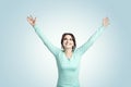 A  brunette girl in a mint-colored jumper stands against the blue background o The young woman raised her hands up Royalty Free Stock Photo