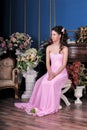 Brunette girl in a pink elegant dress among the flowers in the room