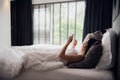 Brunette girl is reading text message from her boyfriend on mobile, while is lying in the bed. Cheerful young woman Royalty Free Stock Photo