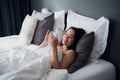 Brunette girl is reading text message from her boyfriend on mobile, while is lying in the bed. Cheerful young woman Royalty Free Stock Photo