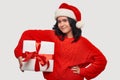 Brunette girl in a red sweater and Santa Claus hat holding white giftbox with red ribbon Royalty Free Stock Photo