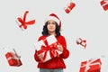 Brunette girl in a red sweater and Santa Claus hat holding white giftbox with red ribbon Royalty Free Stock Photo