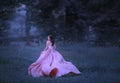 A brunette girl runs in a forest that has shrouded in mist. A lady in a pink flying, waving, long dress with a train