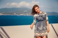 brunette girl in short grey frock smiles by wall against sea