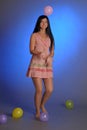 Brunette girl in a short pink dress with balloons plays on a blue background in the studio