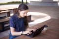 A brunette girl sits behind wooden desk, looks at a laptop monitor, smiles, laughs, talks online, drinks coffee, works. Royalty Free Stock Photo