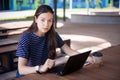 A brunette girl sits behind wooden desk, looks at a laptop monitor, smiles, laughs, talks online, drinks coffee, works. Royalty Free Stock Photo