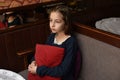 Scared young woman is watching tv. Brunette girl is sitting on the couch with red pillow