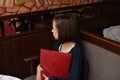 Scared young woman is watching tv. Brunette girl is sitting on the couch with red pillow