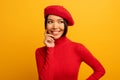 Brunette girl smiles with red hat and cardigan. Emotional and joyful expression. Yellow background