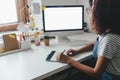 Brunette girl in striped shirt drawing on graphic tablet and looking at computer screen. Indoor photo of young woman Royalty Free Stock Photo