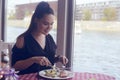 Brunette girl with a tail sitting in a restaurant on ship on the background of the river. Girl tries salmon with rice. Girl eats a Royalty Free Stock Photo