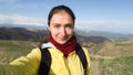 Brunette girl takes a selfie on a smartphone on the background of the field and mountains. On the shoulders of the backpack.