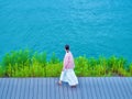 Brunette girl in a white skirt and pink jacket walking on a wooden pier path near the water Royalty Free Stock Photo