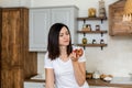 Brunette girl in a white T-shirt in the kitchen eat an apple. Royalty Free Stock Photo