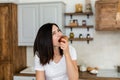 Brunette girl in a white T-shirt in the kitchen eat an apple. Royalty Free Stock Photo