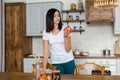 Brunette girl in a white T-shirt in the kitchen eat an apple. Royalty Free Stock Photo