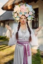 Brunette girl in a white ukrainian authentic national costume and a wreath of flowers is posing against a white hut Royalty Free Stock Photo