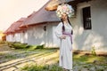 Brunette girl in a white ukrainian authentic national costume and a wreath of flowers is posing against a white hut. Royalty Free Stock Photo